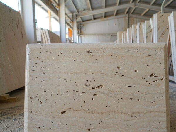 A bullnosed travertine pool coping with a drop edge, on bearers in a stone yard