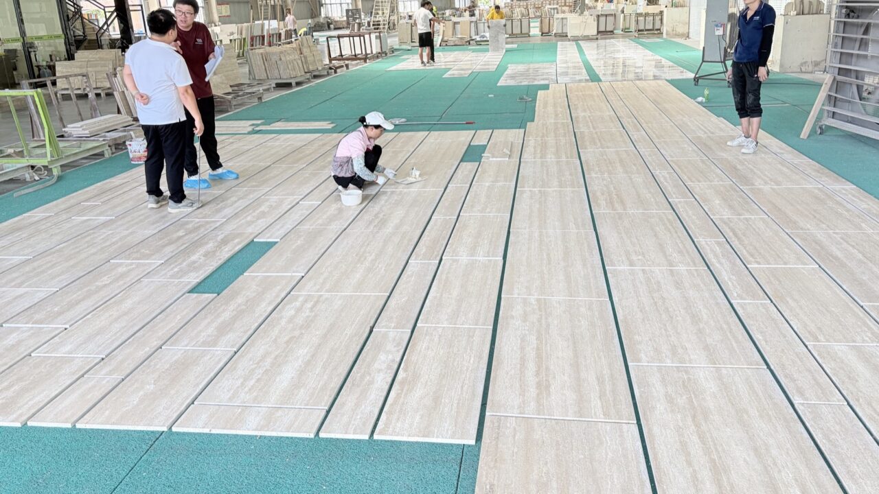 Four people standing and crouching over long travertine slabs laid out across a workshop floor for inspection