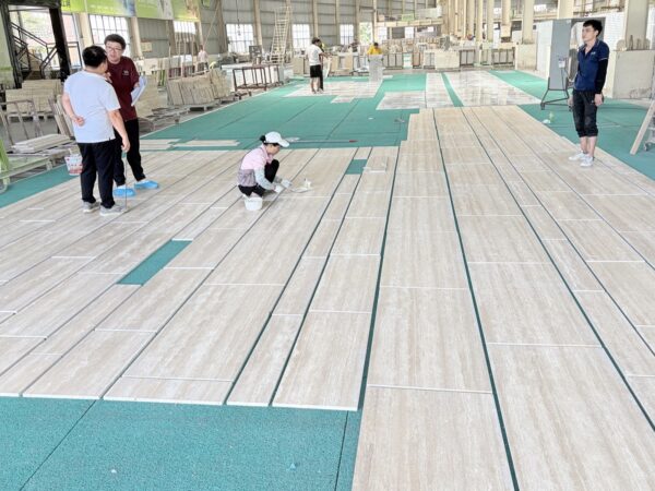 Four people standing and crouching over long travertine slabs laid out across a workshop floor for inspection