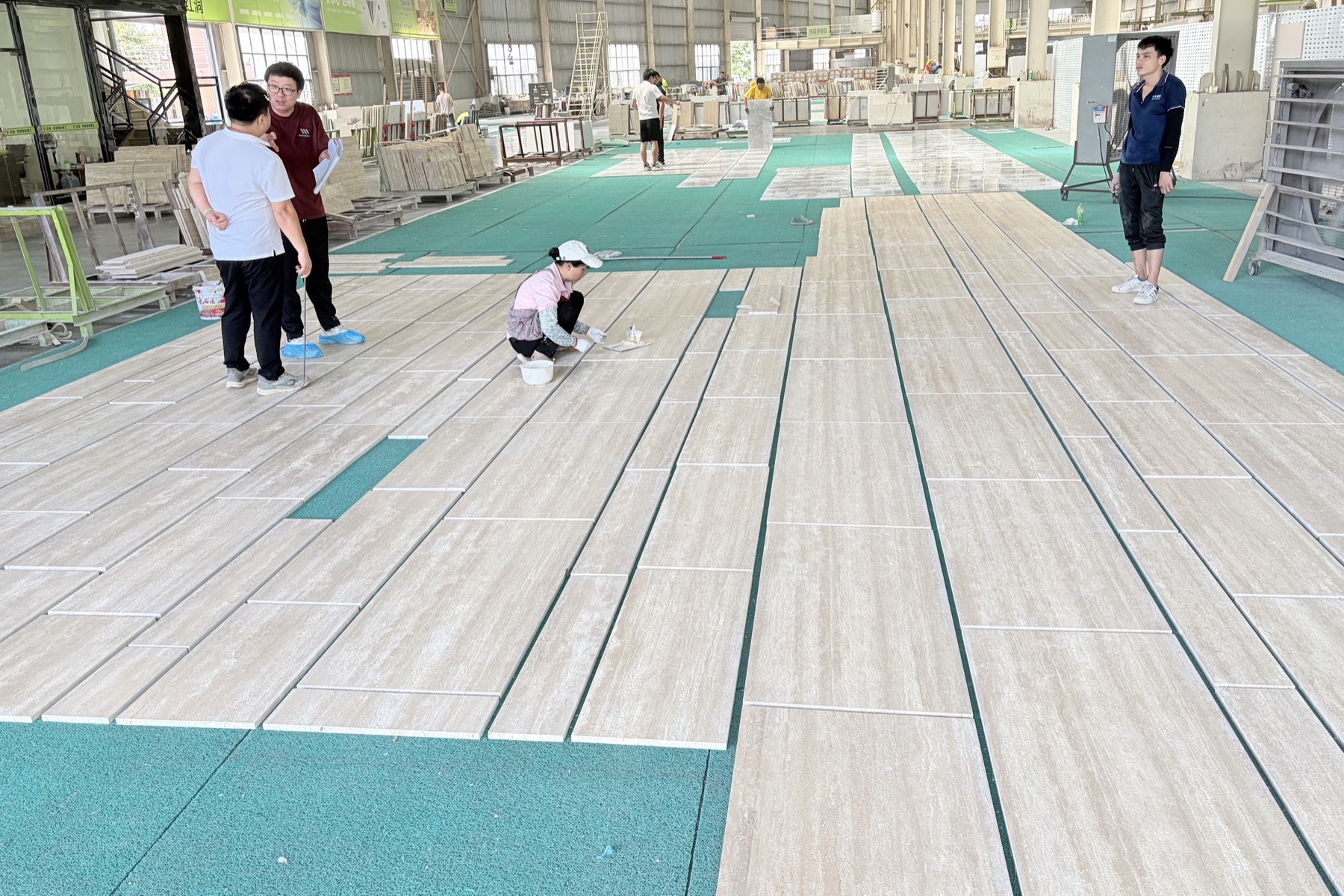 Four people standing and crouching over long travertine slabs laid out across a workshop floor for inspection