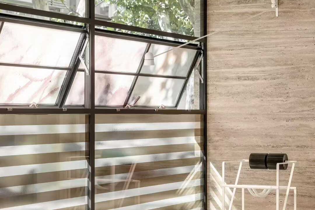 Travertine cladding wrapping an internal corner beside a steel-framed window