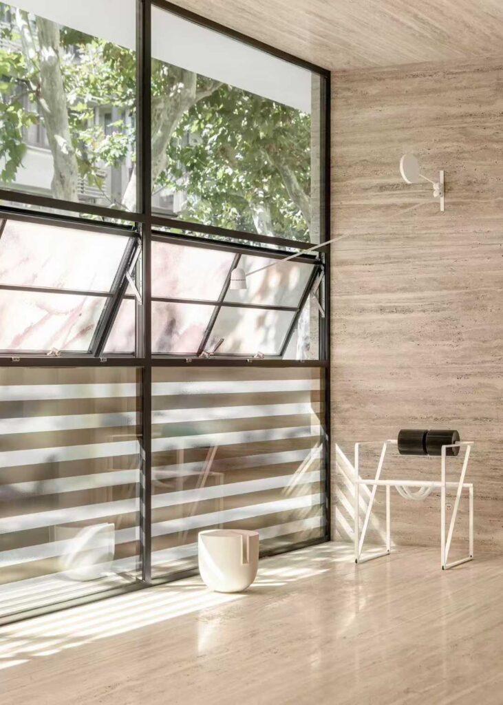 Travertine cladding wrapping an internal corner beside a steel-framed window
