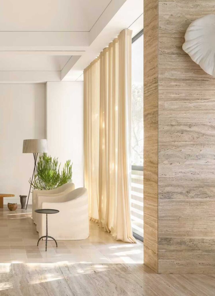 A travertine counter beside a timber chair and framed pictures on a white gallery wall
