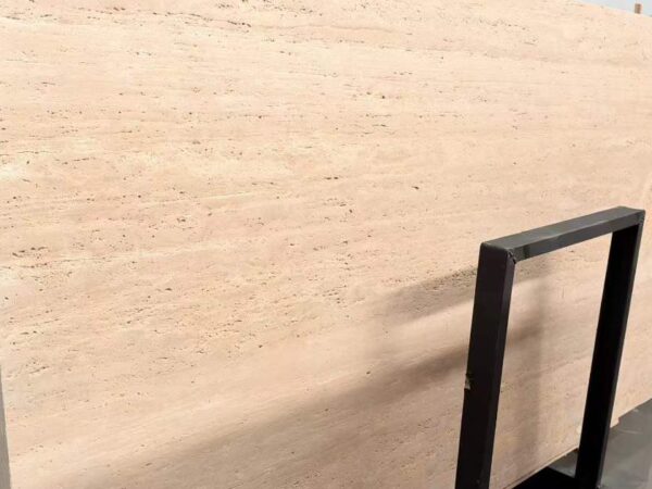 A tall travertine slab leaning in a storage rack, its cut face showing fine horizontal layering